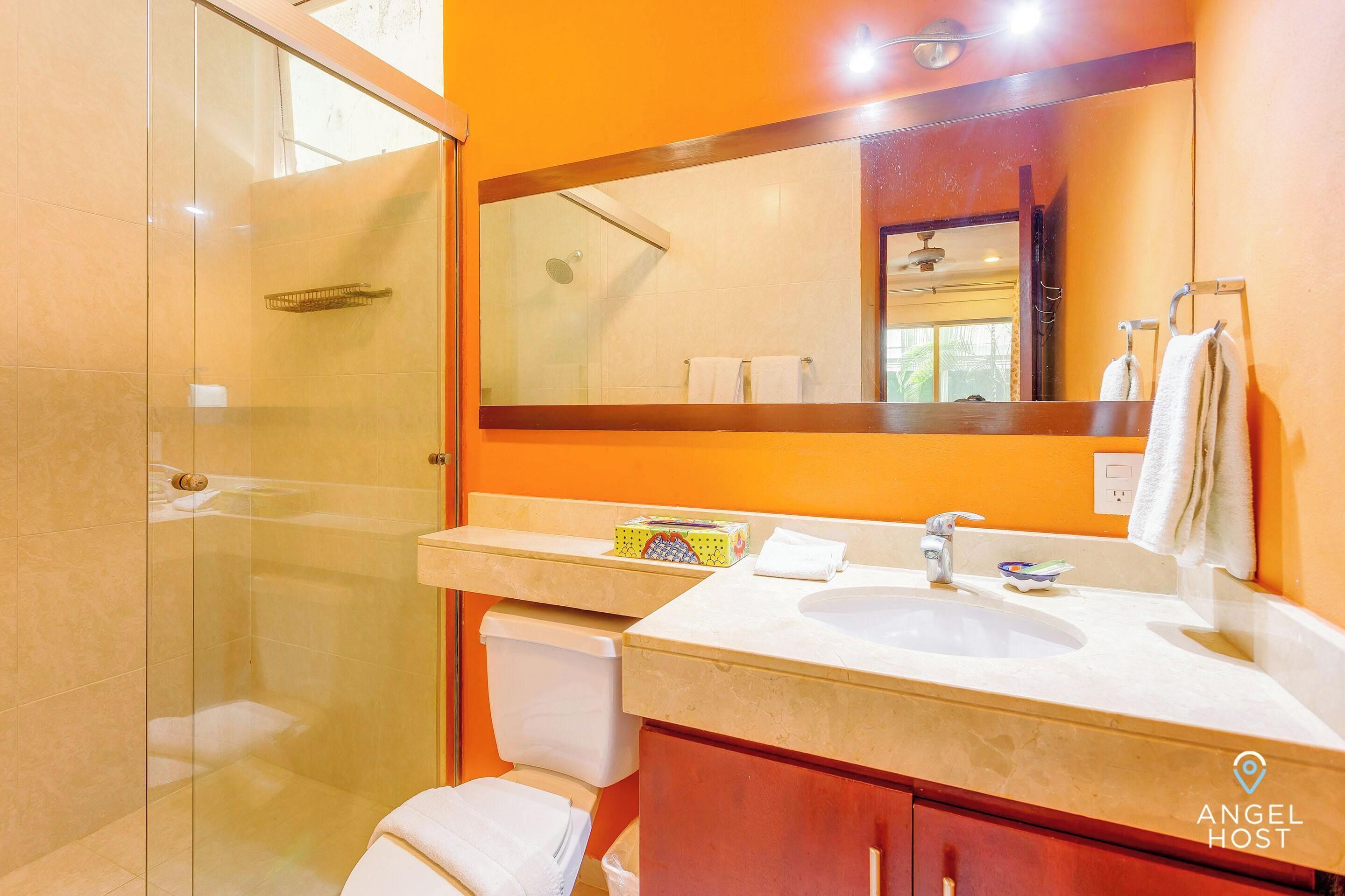 Un baño con cabina de ducha de vidrio, un lavabo, un espejo y un perchero para toallas.