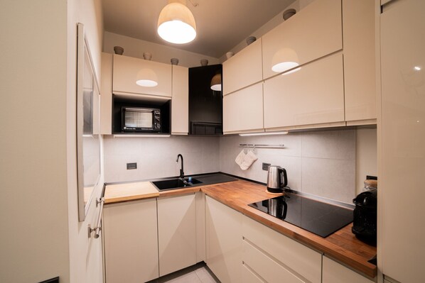 A modern kitchen with white cabinets, a black countertop, a microwave, a sink, and a kettle.