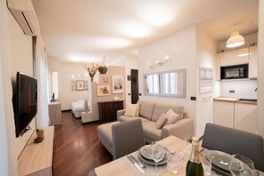 A modern living room with a sofa, dining table set for two, and a kitchen area with a microwave.