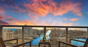 A balcony with a city view, a table with bottles and fruit, and a sunset sky.