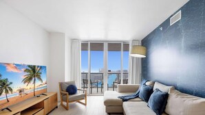 Een moderne woonkamer met een groot raam, een bank, een fauteuil, een televisie en een balkon met uitzicht op de stad.