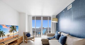 A modern living room with a TV, a sofa, a chair, and a balcony with a city view.