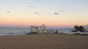 A beach with a white building featuring a dome and multiple arches, overlooking the sea. - Cosy Apartment in La Marsa Corniche (Site archéologique de Carthage)