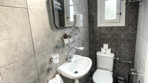 A modern bathroom with a white sink, toilet, and a mirror above the sink. There is a window with a towel rack above it, and a small potted plant on the wall. - Cosy Apartment in La Marsa Corniche (Site archéologique de Carthage)