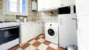 A compact kitchen with white cabinets, a stove, a washing machine, and a refrigerator. - Cosy Apartment in La Marsa Corniche (Site archéologique de Carthage)