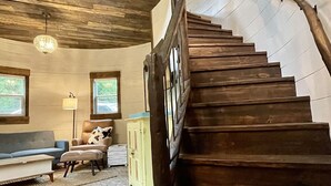 A rustic interior with a wooden staircase, a sofa, a lamp, and a view of the outdoors.