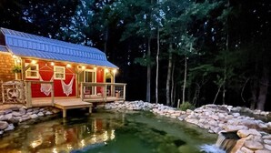 A cabin with a small pond, surrounded by trees.