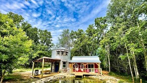 A rustic cabin with a small porch and a pond in front.