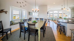 A spacious dining area with a long table and chairs, a chandelier, and a view of the sea through large windows.
