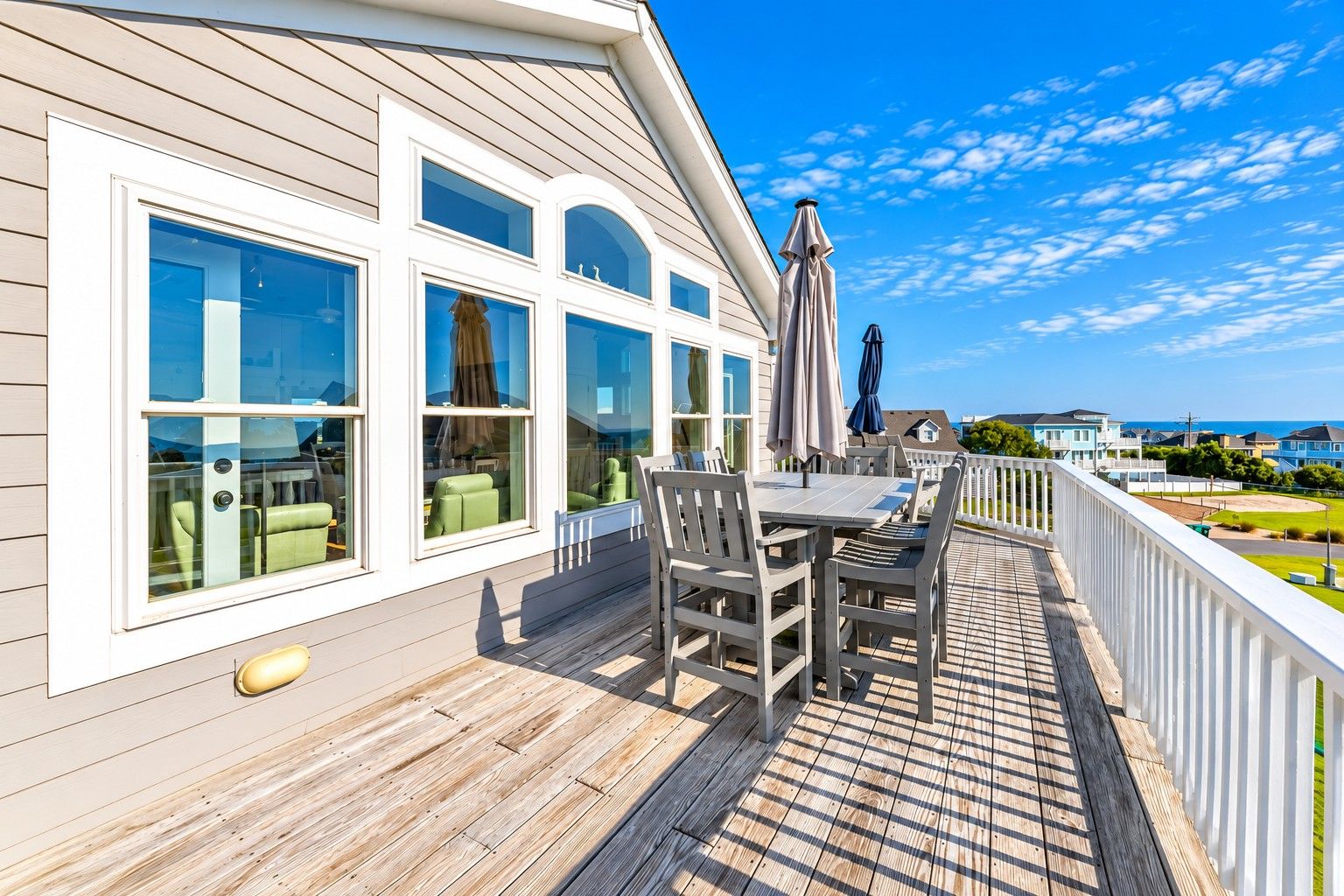 A wooden deck with a table and chairs, large windows, and a view of the sea.