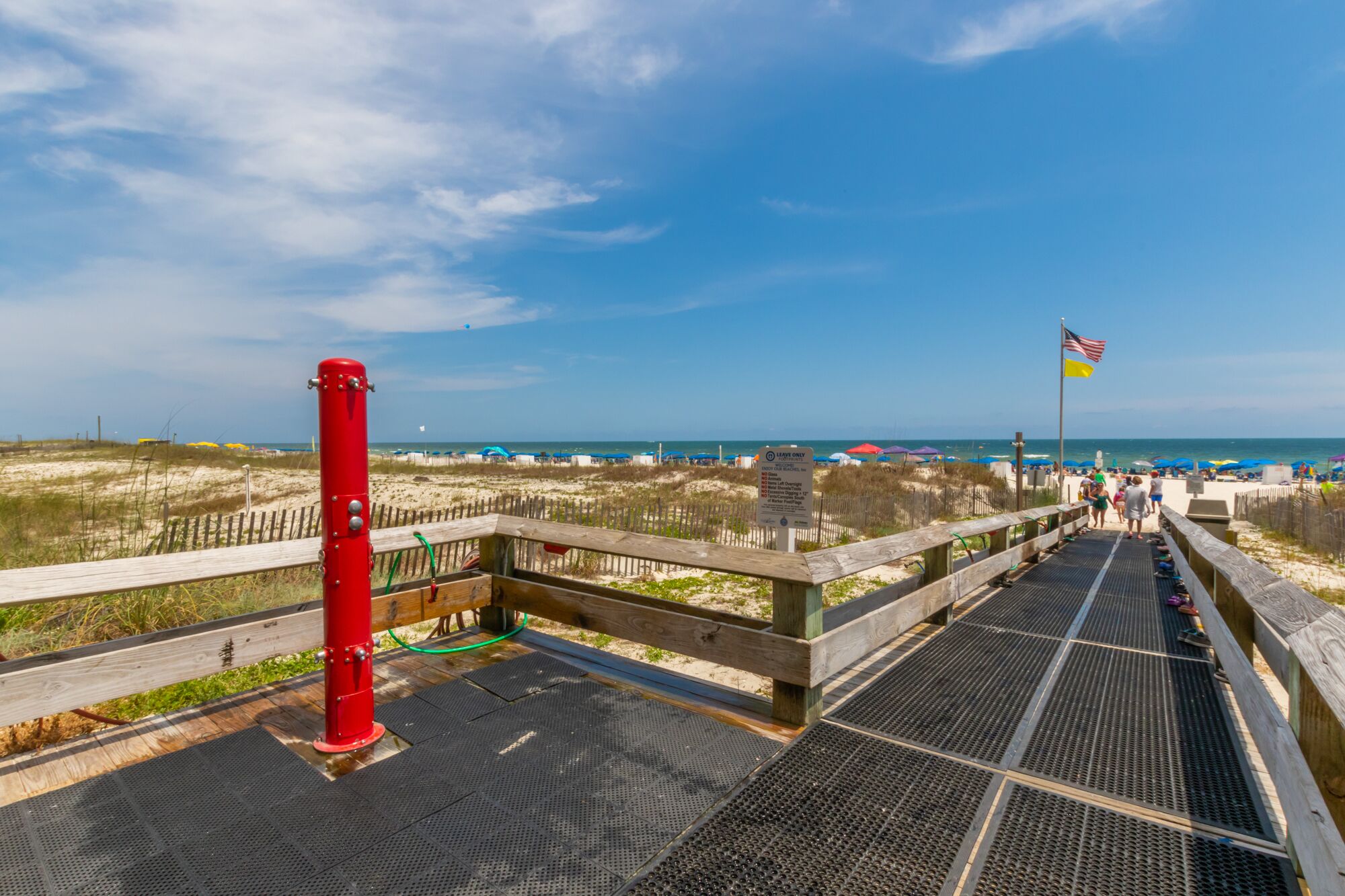 A wooden boardwalk leading to a beach with a red fire hydrant and a 'Leave Only Trash' sign.
