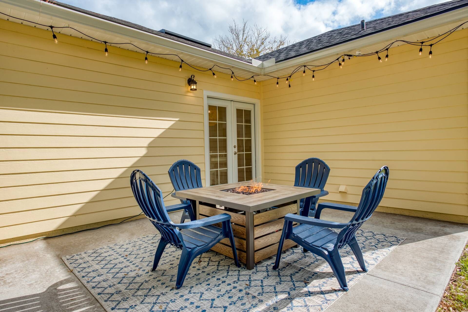 A patio with a table and four chairs, a fire pit, and string lights.