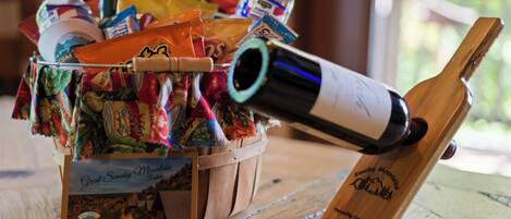 A wooden table with a basket containing snacks, a bottle of water, a bottle of wine, and a wooden wine opener.