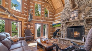A log cabin interior with a stone fireplace, leather furniture, and a mounted deer skull.