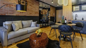 A modern living room with a sofa, coffee table, and dining area with chairs. - Apartament CHICAGO (Nowy Targ)