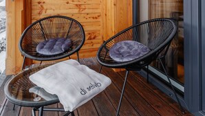 A wooden cabin with two black wicker chairs with cushions, a white table with a bag, and a glass door leading outside. - Apartament CHICAGO (Nowy Targ)