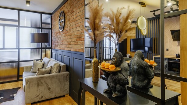 A modern living room with a sofa, a dining table, and decorative items including a vase and a sculpture of a gorilla. - Apartament CHICAGO (Nowy Targ)