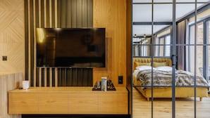 A modern bedroom with a large bed, a TV mounted on a wooden panel, and a bedside table with books and a lamp. - Apartament CHICAGO (Nowy Targ)