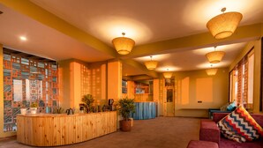 Una zona de recepción con mostrador de madera, plantas en macetas y un área de descanso con cojines de colores.
