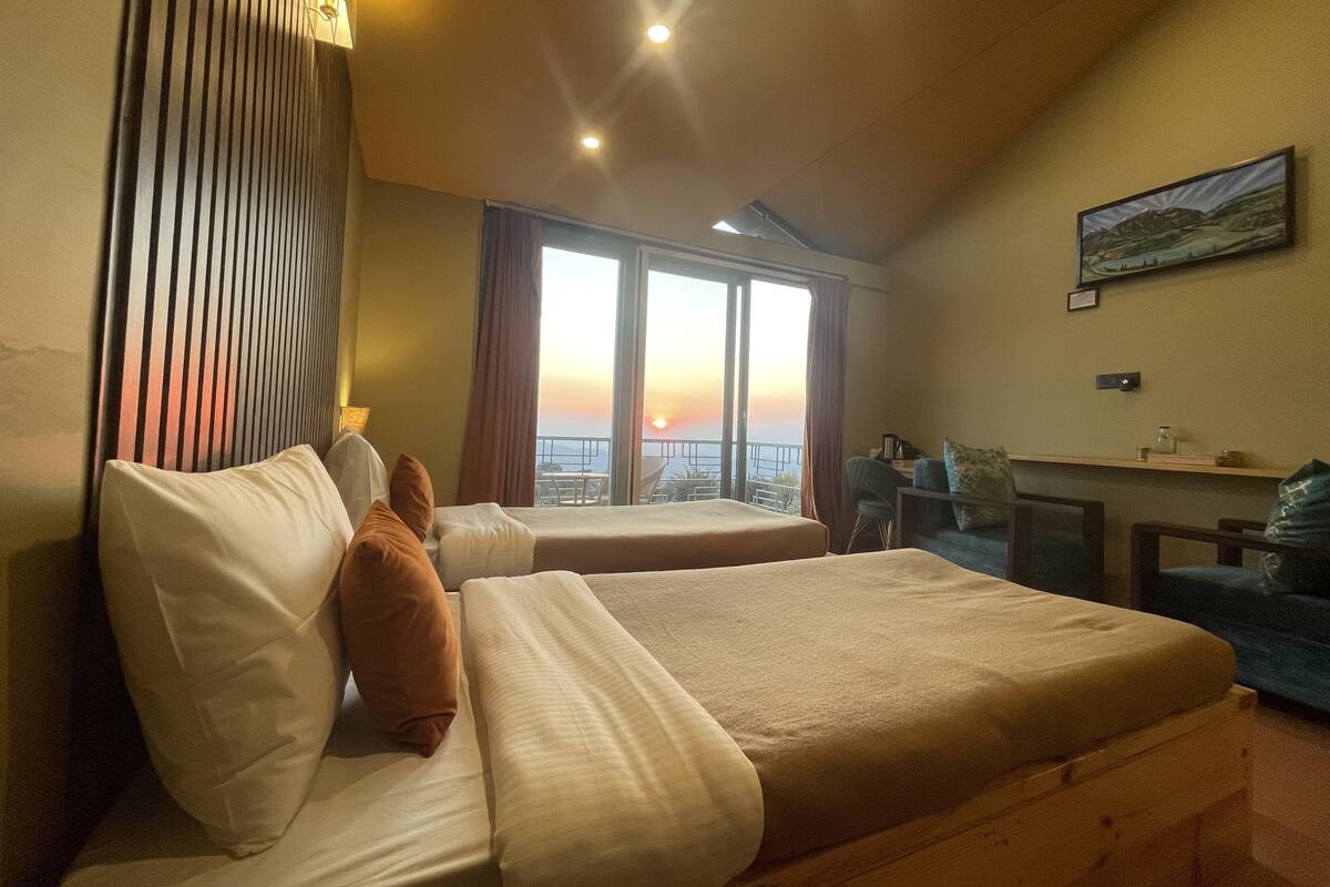 Une chambre d’hôtel avec deux lits, un bureau, une chaise et une grande fenêtre donnant sur un magnifique coucher de soleil.
