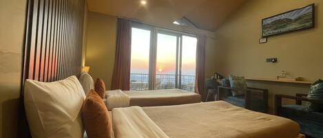 A hotel room with two beds, a desk, a chair, and a large window with a sunset view.