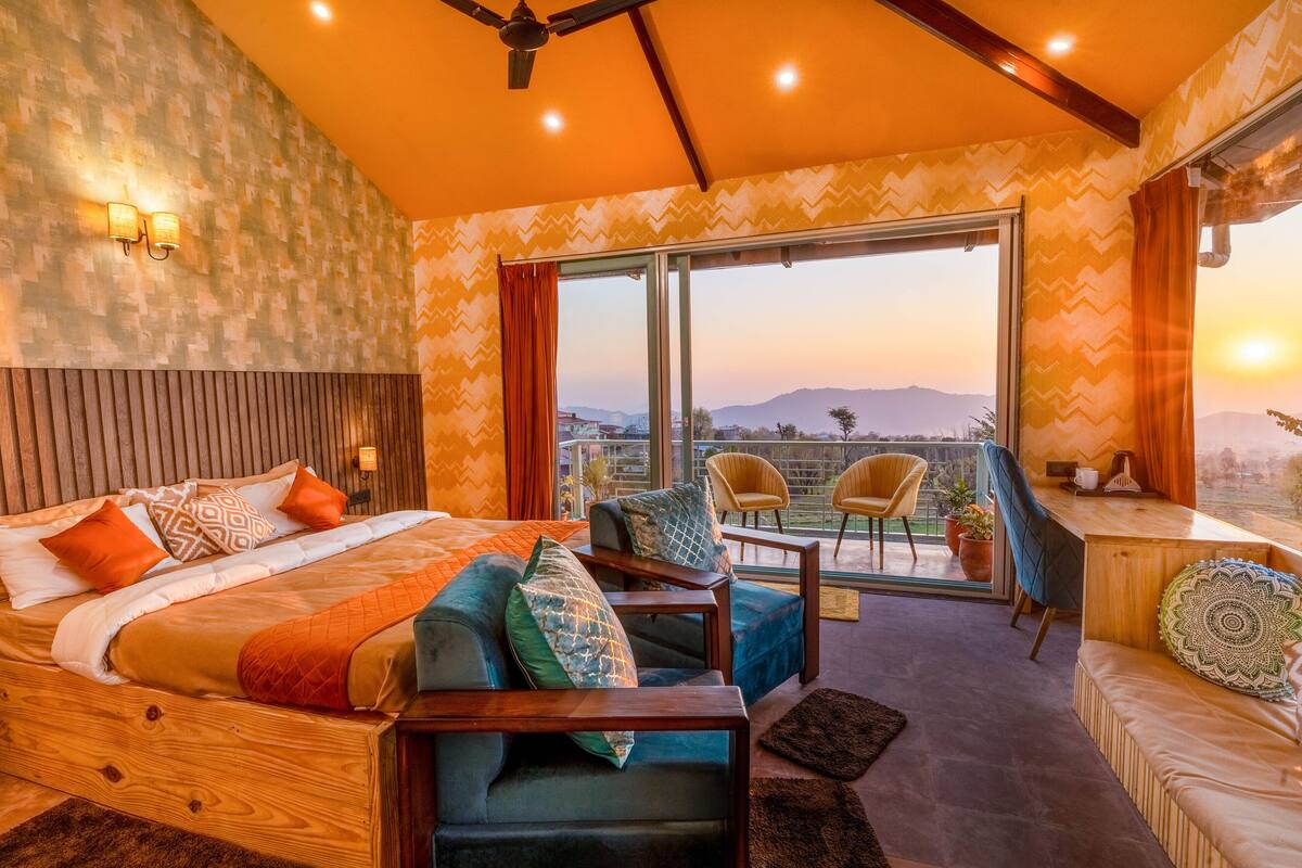 Une chambre avec un grand lit, un balcon avec des chaises et une vue sur les montagnes.