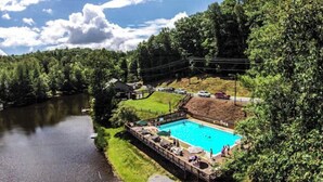 Una piscina con plataforma de madera, rodeada de árboles y un río.