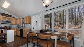 Una cocina con armarios de madera, microondas, estufa y un ventanal con vistas a árboles.