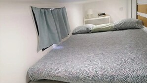 Ein Schlafzimmer mit einem Bett, einem Nachttisch, einer Lampe und einem Fenster mit Vorhängen.