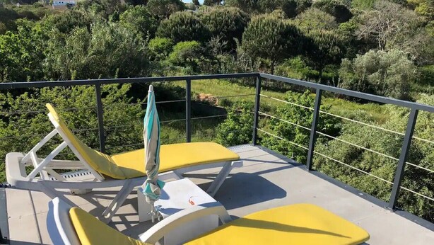 Ein Balkon mit zwei gelben Liegestühlen und einem kleinen Tisch, umgeben von einem Metallgeländer.