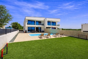 Uma casa moderna de dois andares com piscina, área de estar externa e gramado bem cuidado.