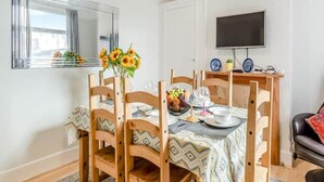 A dining area with a wooden table set for four, a mirror, and a television on the wall.