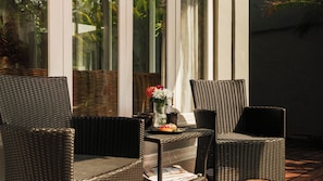 Un ensemble de meubles de jardin en osier, comprenant une chaise et une table, est installé sur une terrasse, agrémenté d’un vase de fleurs et d’une assiette de nourriture.