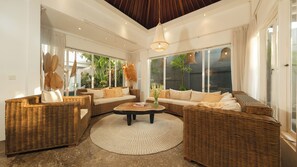 A spacious living area with wicker furniture, large windows, and a central coffee table.