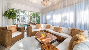 A spacious living area with wicker furniture, a wooden coffee table, and a large window with sheer curtains. - Villa Moana Canggu by Villa Finder (Canggu)