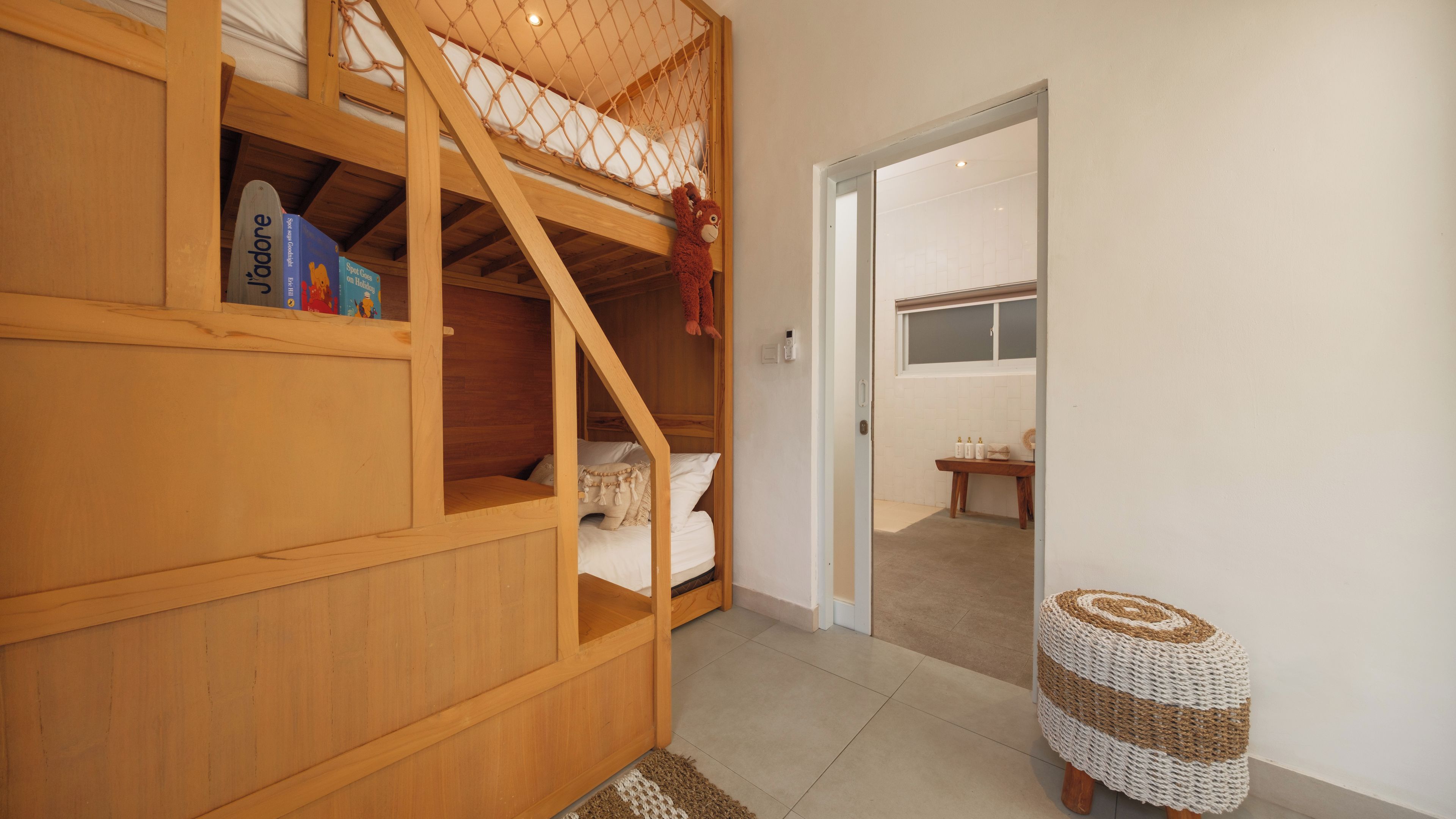 A room with a bunk bed, a small table with bottles, and a woven stool.