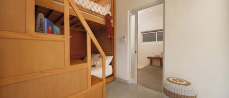 A room with a bunk bed, a small table with bottles, and a woven stool.