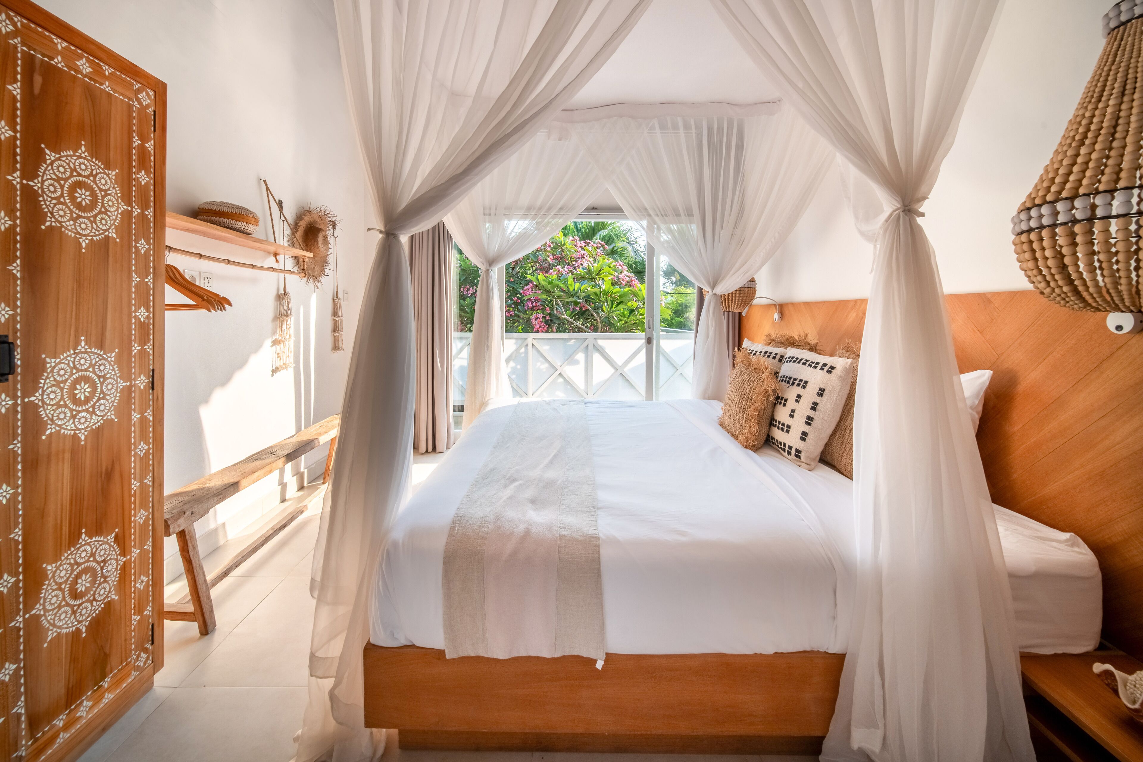 A bedroom with a large bed, a wooden wardrobe, and a view of greenery outside.