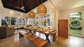 Amplia sala de estar con una gran mesa de comedor de madera, muebles de mimbre y un ventilador de techo.
