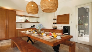 Un coin repas avec une table en bois mise pour le petit-déjeuner, un distributeur d’eau et une vue sur l’extérieur.