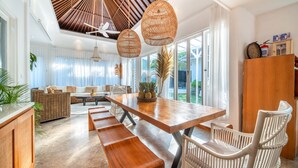 A modern dining area with a wooden table, white wicker chairs, and a bench. - Villa Moana Canggu by Villa Finder (Canggu)