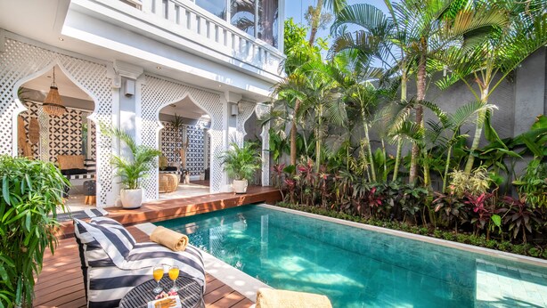 A poolside area with lounge chairs, a small table with drinks, and lush tropical plants. - Villa Moana Canggu by Villa Finder (Canggu)