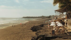 Una spiaggia con una struttura a tetto di paglia, tavoli e sedie in legno.