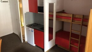 Een compacte kamer met een kitchenette, stapelbedden en een deur naar een andere kamer.