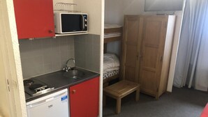 Een compacte keuken met een magnetron, spoelbak en een kleine koelkast. Er is een houten bankje en een stapelbed in de kamer.