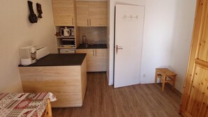 Een kleine keuken met houten kastjes, een klein aanrecht en een koelkast.