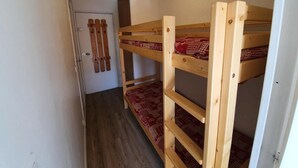 Een smalle kamer met stapelbedden en een deur.