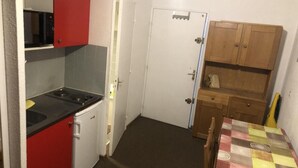 Una cocina compacta con microondas, un refrigerador pequeño y un lavamanos. Hay un armario de madera y una mesa con mantel estampado.
