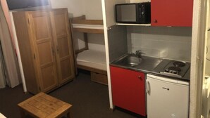 Cocina compacta con microondas, lavamanos y estufa. Hay una mesita pequeña y una cama litera en la habitación.