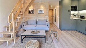 A modern living room with a wooden staircase, a grey sofa, a coffee table, and a kitchen area with grey cabinets and a microwave. - 10m from ski slopes, 4th floor, 62m², Méribel-Mottaret (Méribel - Les Allues)